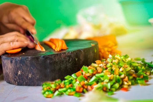 Hands cutting carrot pieces on a homemade chopper. Close up of hands chopping carrots in a wooden chopper. Concept of hands cutting vegetables in a wooden chopper