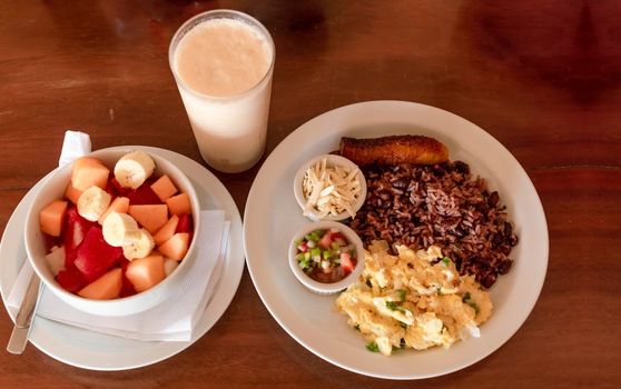 Gallo pinto breakfast served on the table with a fruit salad, Traditional gallopinto dish with fried eggs and a bowl of fruit salad on the table. Traditional gallo pinto served at the table