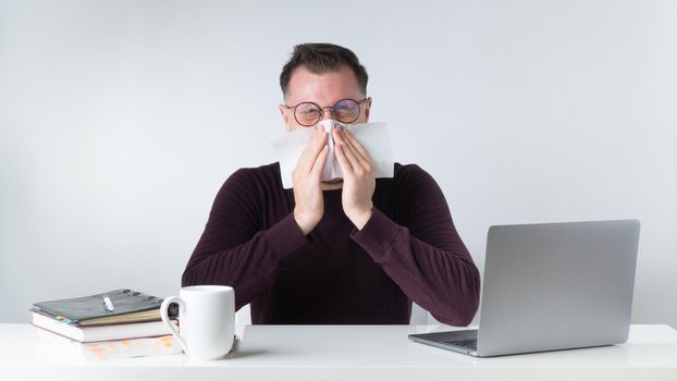 A man sneezes or blows his nose at the workplace in the office. High quality photo