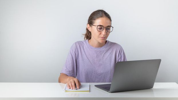 A female student sits at a laptop with a notebook and a pen. High quality photo