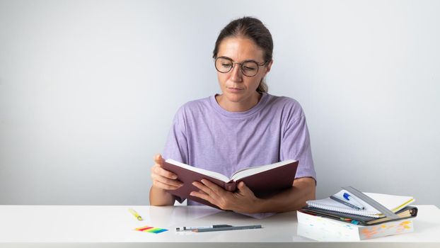 A student girl reads a book at a study table with notebooks and pens. High quality photo