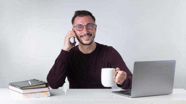 A man works at a laptop with a phone in his hand and a cup of coffee. High quality photo