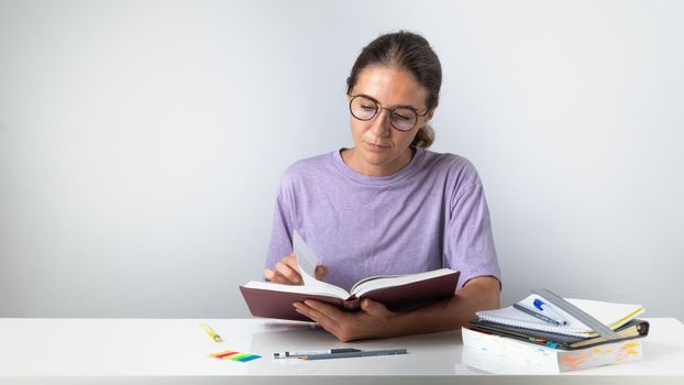 Studying the material, a student with glasses reads a textbook at the table. High quality photo