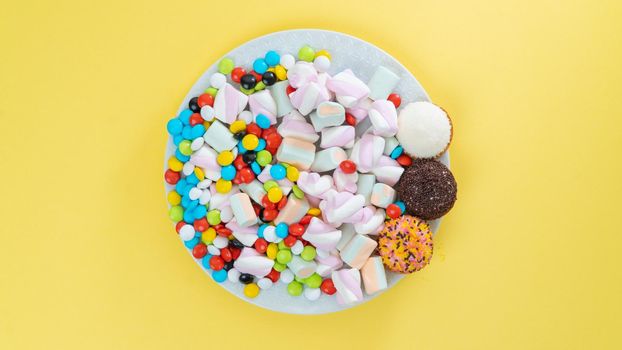 Colorful sweets, marshmallows, cakes, dragees and sweets on a bright yellow background. High quality photo