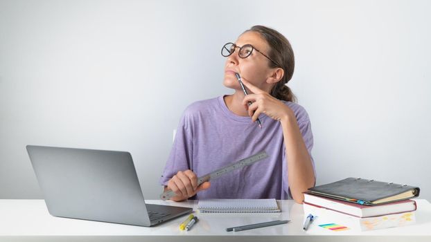 A girl with a laptop with a pile of books and notebooks on the table with a pensive look. High quality photo