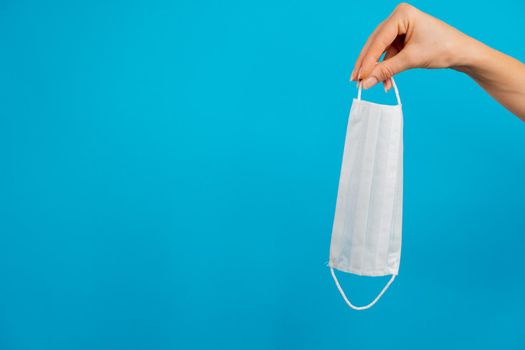 A woman's hand holds a white mask on a blue background, space for text. High quality photo