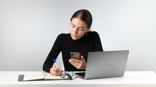 A woman works at a laptop, makes notes in a notebook, planning, routine. High quality photo