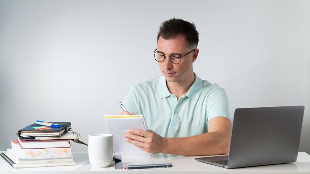 A student writes in a notebook - on the table books, textbooks, laptop. High quality photo