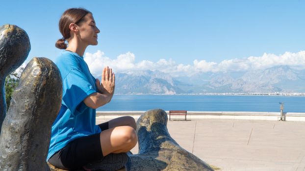 A woman with namaste hands meditates against the backdrop of the sea and mountains. High quality photo