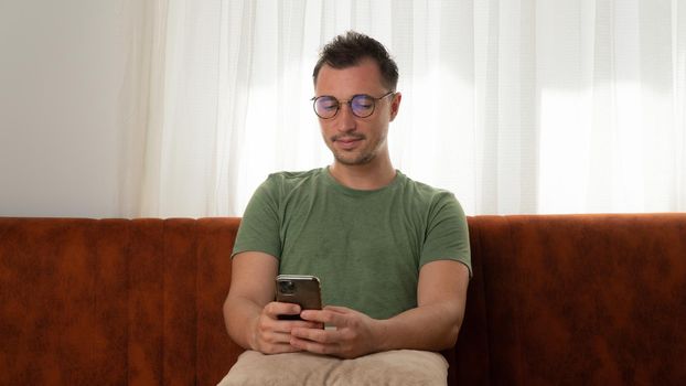 A man with a phone in his hands sits on the couch of the house. High quality photo