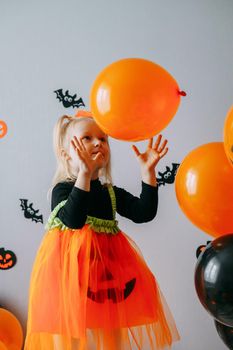 Children's Halloween - a girl in a witch hat and a carnival costume with airy orange and black balloons at home. Ready to celebrate Halloween.