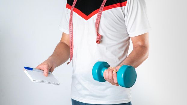 Trainer nutritionist man with dumbbell, notebook and measuring tape sports image. High quality photo