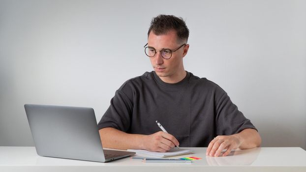 A guy at a laptop makes notes in a notebook at the workplace - work and study. High quality photo
