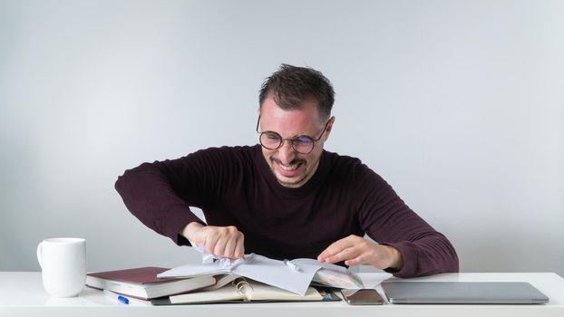 Angry man working in office tears out a piece of paper from a notebook - wrong entries. High quality photo