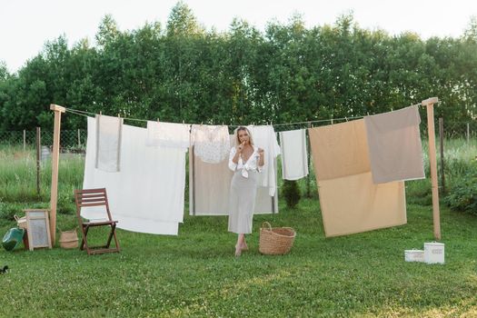 Laundry day. A woman hangs linen and towels on a tree in the courtyard of a village house. Summer cottage concept.