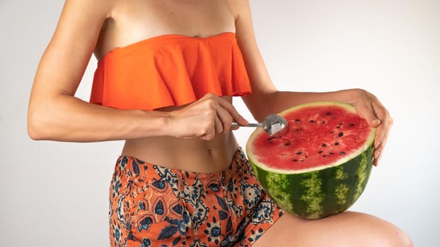 A woman in a swimsuit eats watermelon with a spoon on a white background - summer pace. High quality photo