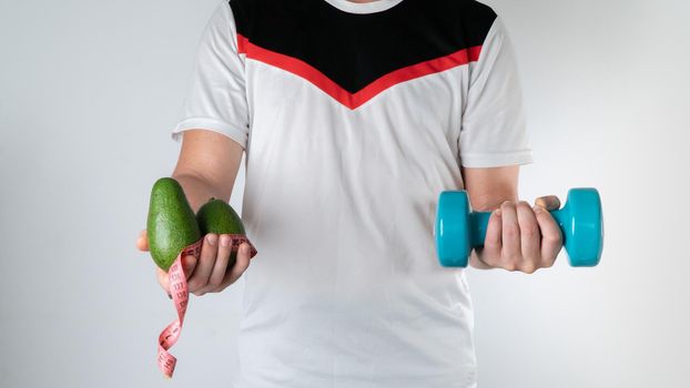 Athletic man with avocado, measuring tape and dumbbells, trainer. High quality photo
