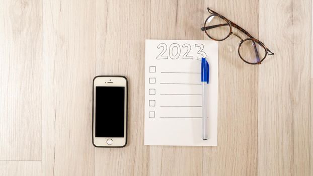 Checklist for 2023, smartphone and glasses on a wooden table, to-do list for the new year. High quality photo