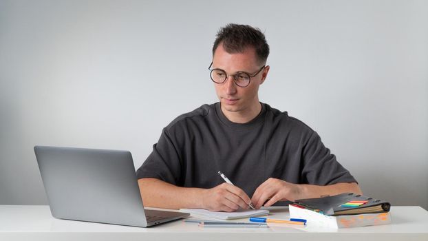 A man at his desk writes in a notebook, looks at a laptop. High quality photo