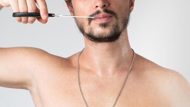 A man with scissors cuts his mustache - body and hair care, haircut and styling beard, close-up