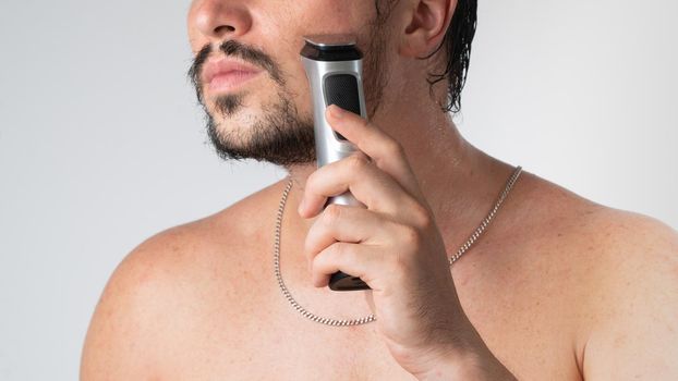A man shaves his beard with a styler trimmer on a white background. High quality photo