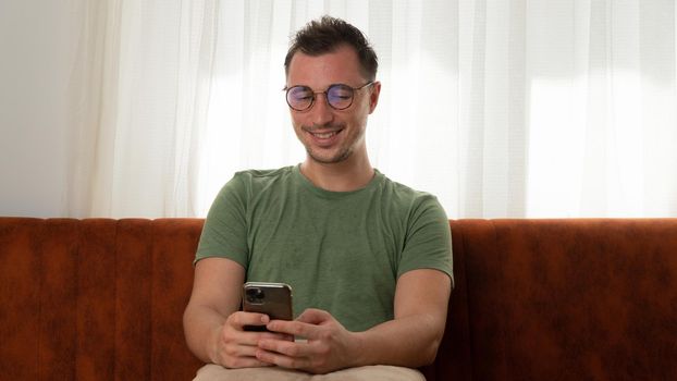 A satisfied man chats in a smartphone from home on the couch. High quality photo