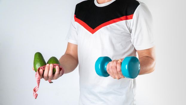 A male trainer holds a dumbbell, avocado and measuring tape for a healthy lifestyle. High quality photo