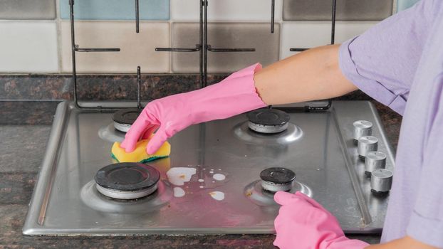 Women's hands in rubber gloves wash a gas stove with a sponge and foam. High quality photo