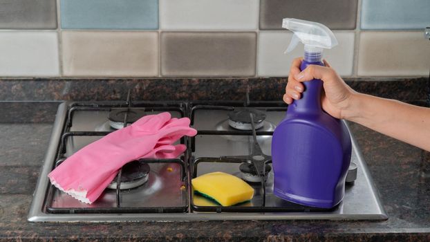 Rubber gloves, sponge and hand holding detergent on the gas stove - cleaning and washing kit