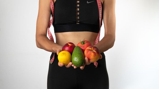 Trainer nutritionist woman holds fruits and vegetables in her hands, measuring tape on the neck - sports, weight loss and proper nutrition. High quality photo