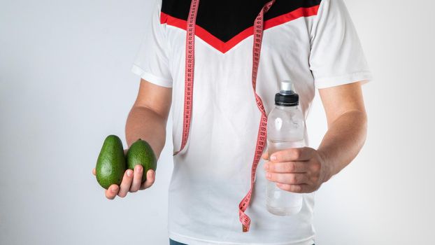 Sporty man with proper nutrition, avocado and water, with measuring tape. High quality photo