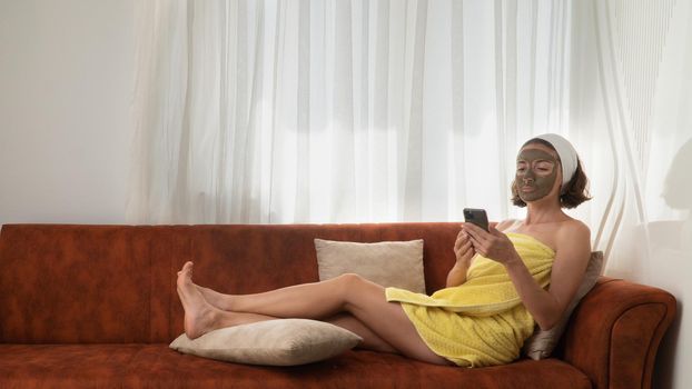 Green cream mask of clay on the face, woman on the couch with a teelphone. High quality photo