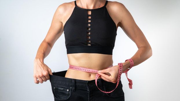 Measuring the waist with a measuring tape - a woman has lost weight, clothes have become larger. High quality photo