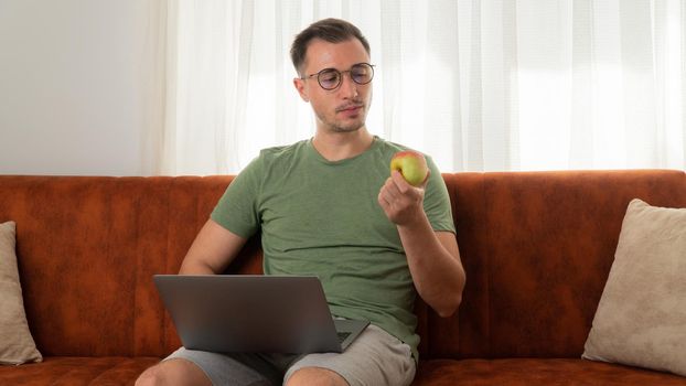 A man eats an apple on the couch with a laptop at work at home. High quality photo
