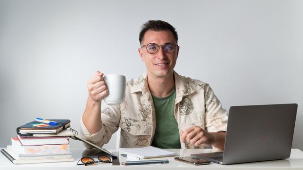 A young man in stylish clothes drinks coffee at his desk - hipster. High quality photo