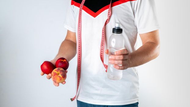 Athletic man holding fruit, a bottle of water and a measuring tape - training plan and healthy eating. High quality photo