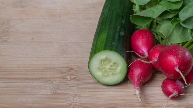 Radishes with leaves and half a cucumber on a background made of wood. High quality photo