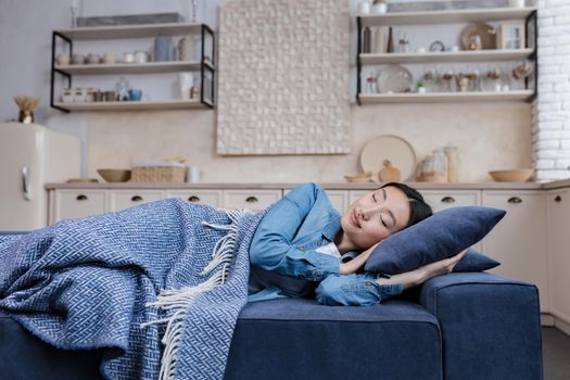 Young beautiful Asian woman resting and sleeping at home lying on sofa under blanket in living room, day nap