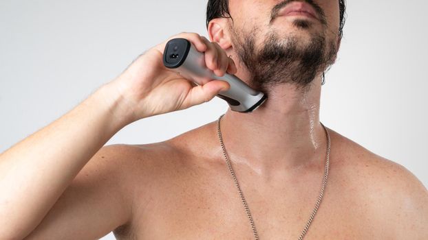 A man shaves his beard with a styler trimmer - self-care at home. High quality photo