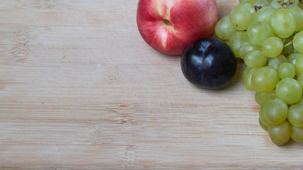 A bunch of grapes, plums and nectarine on a wooden background with a place under the text. High quality photo