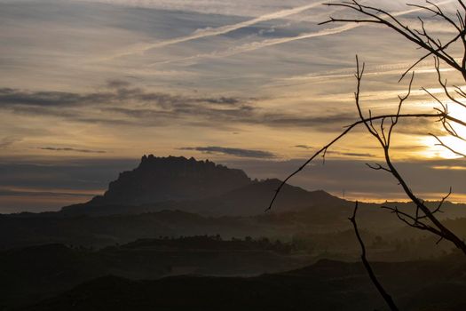 Beautiful landscape showing Montserrat mountain under a cloudy sky and some branches in the foreground