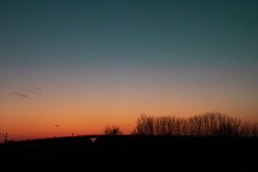 Landscape showing the silhouette of a line of trees with a color gradient in sunset