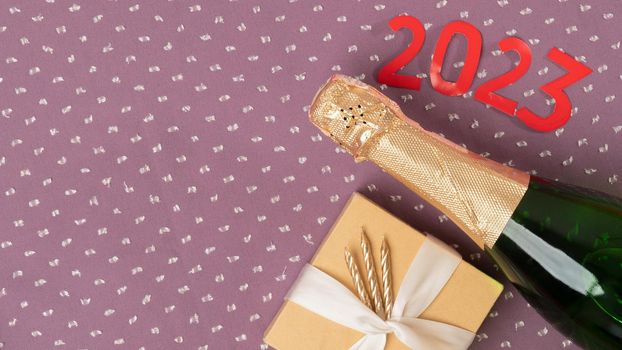 The number 2023 in red, champagne and a New Year's gift on a purple background. High quality photo