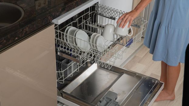 Housewife takes clean cups out of dishwasher