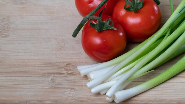 tomatoes on a branch and green onions, vegetables and greens on a wooden background. High quality photo