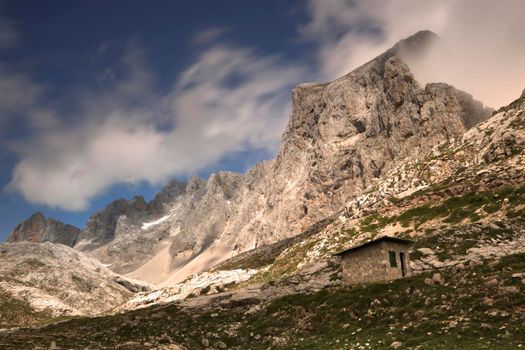 Landscape showing mountains and a small refuge under a cloudy sky in Fuente De in Spanish Picos de Europa mountain range