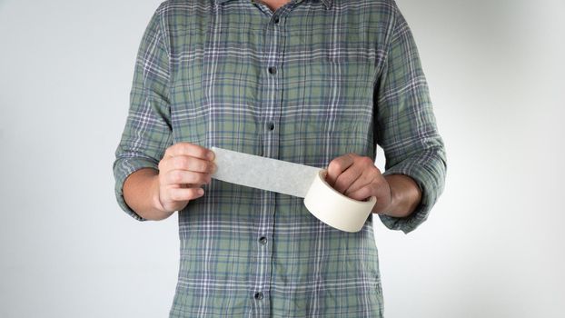 A man tears off a ribbon of white wide tape on a white background. High quality photo