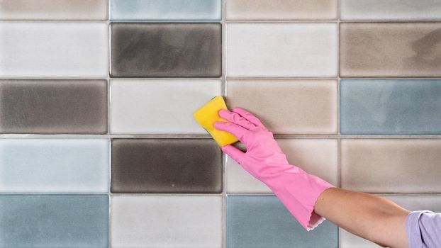 A woman's hand in rubber gloves washes tiles with a sponge. High quality photo
