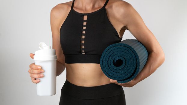 A woman in a sports uniform with a yoga mat and shaker - training. High quality photo