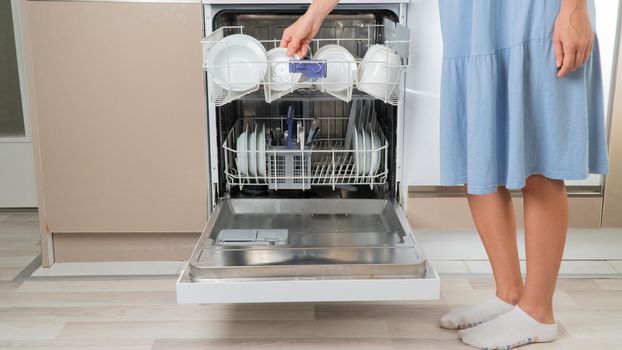 Housewife takes clean plates out of dishwasher